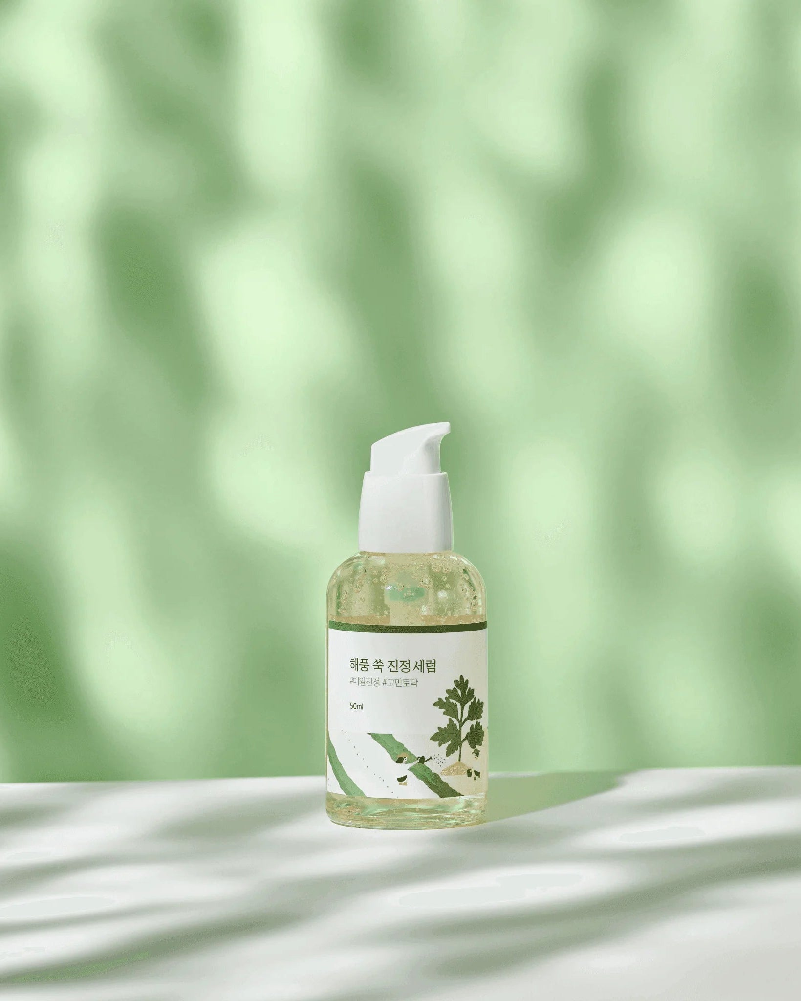 Bottle of skincare product with a green leaf design on a white surface with a blurred green leaf background