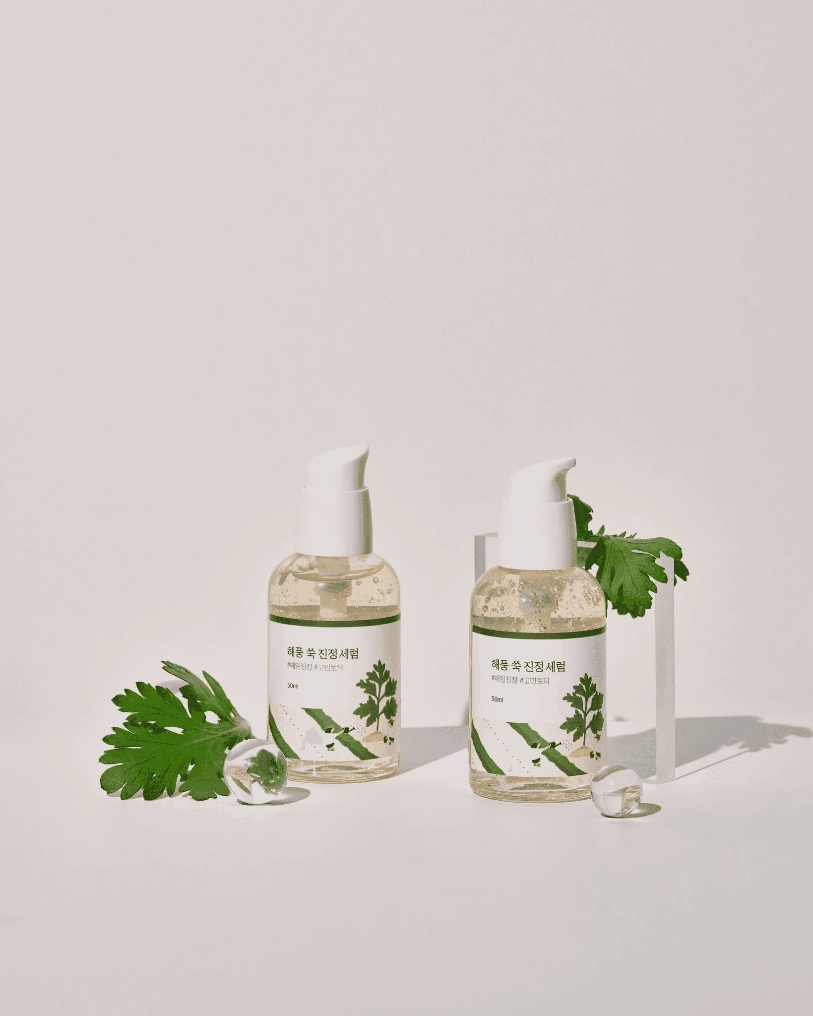 Two glass bottles with green leaves on a light gray background