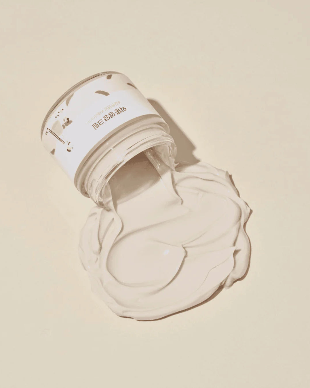 Open jar of cream with a swatch on a beige background